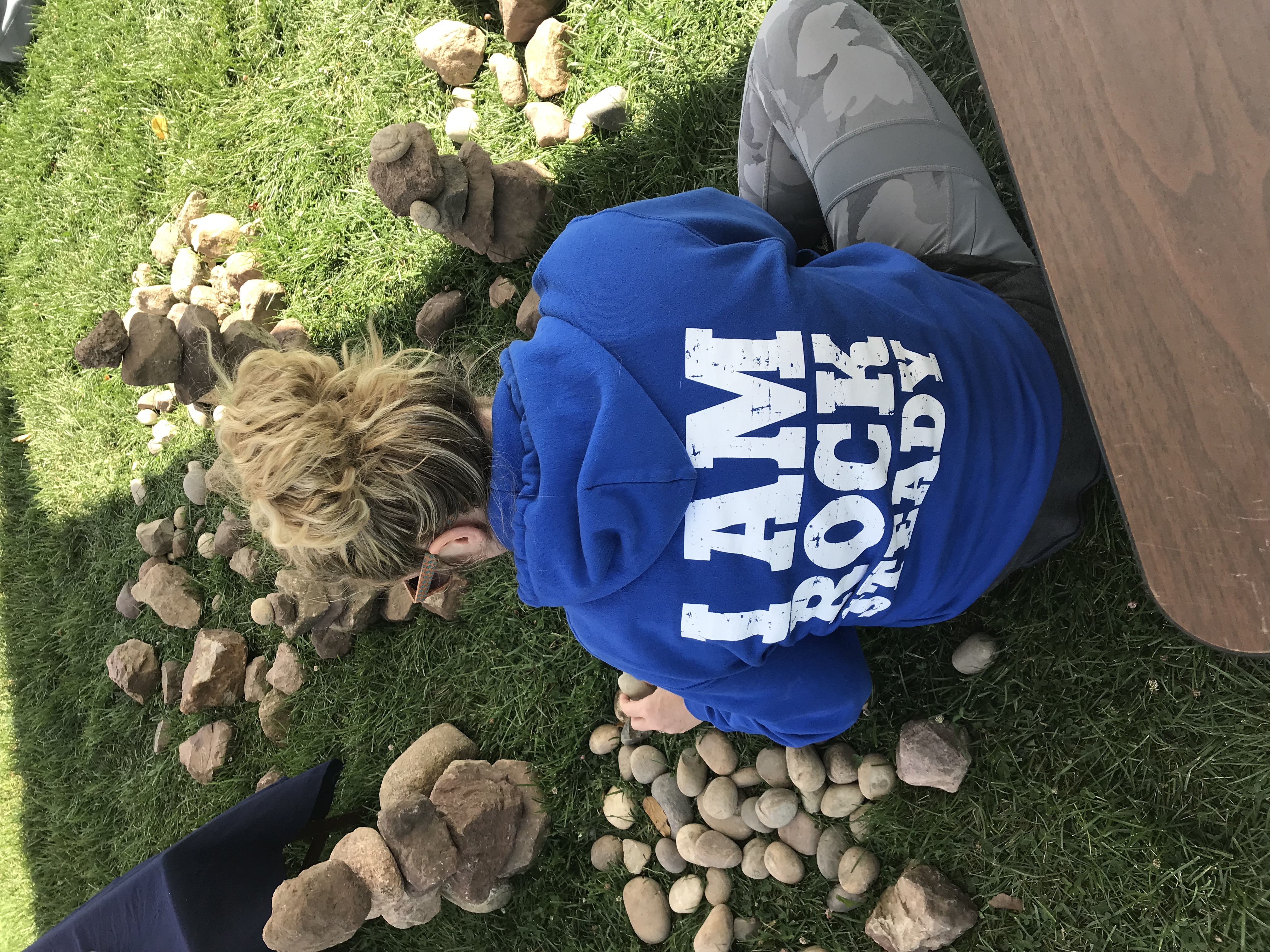Person in an I Am Rock Steady hoodie stacking stones on grass